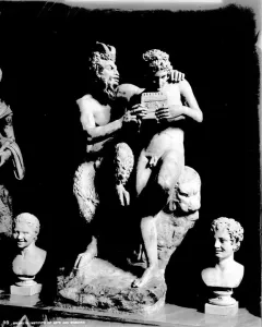 Pan and Daphne marble sculpture showing a bearded, horned figure embracing a nude youth holding a small musical instrument.