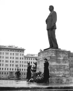 Statue of Joseph Stalin on a stone pedestal, flanked by two armed guards and decorated with flowers.