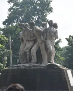 Anti Terrorism Raju Memorial Sculpture with several male figures in forward-moving poses on a dark pedestal, framed by trees.