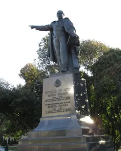 Bronze statue of Benito Juarez standing on a multi-tiered stone pedestal, holding papers and pointing forward.