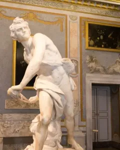 David marble statue in a gilded gallery, shown in a dynamic twisting pose with sling and draped cloth.