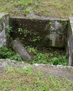 Sunken stone Etruscan tomb structure with moss and weeds growing over the weathered blocks.