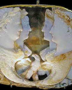 Gemma Claudia cameo with four profile portraits facing inward, gold border, and intertwined horn-shaped elements at the bottom.