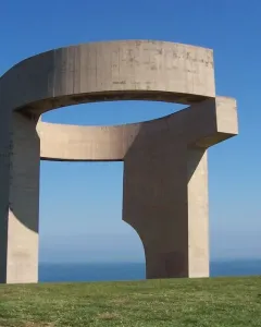 Elogio del Horizonte, a large concrete sculpture with a curved opening, standing on a grassy slope above the sea.