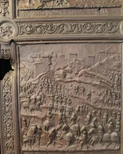 Close-up of the Bronze Gate showing a bas-relief battle scene with soldiers, horses, and a fortified city.