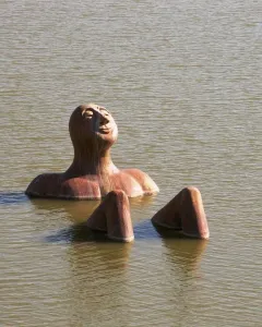 Hombre Río sculpture emerging from calm water with a peaceful face.