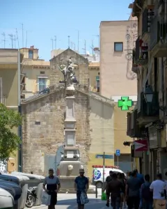 Font de Santa Eulàlia, a tall stone fountain monument in a city square with people seated around its base.