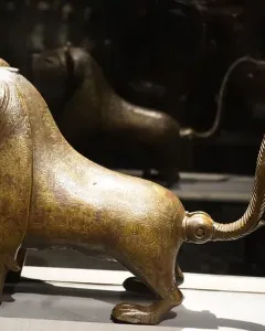 The Lion of Monzon sculpture shown from a three-quarters angle, with engraved decorative patterns across its body.