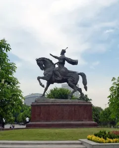 Timur Equestrian Statue on a reddish-brown pedestal in a green park with trees and flowering shrubs.