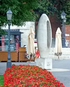 Zero Kilometre Stone sculpture beside a bed of red flowers with buildings and streetlights in the background.