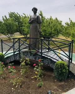 Bronze statue of Zabel Yessayan holding a book on a small arched bridge in a circular garden bed.