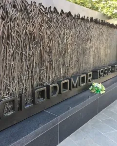 Holodomor Memorial wall with wheat stalk relief and flowers placed below the HOLODOMOR 1932-1933 inscription.