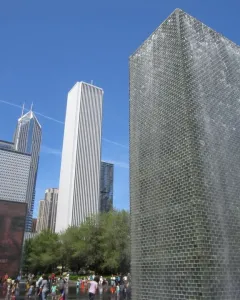 Crown Fountain with water cascading down one tower and a projected face on the other, with people gathered in the shallow pool below.