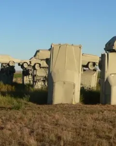 Carhenge sculpture made of tan-colored cars standing in a dry grassy field under a clear blue sky.