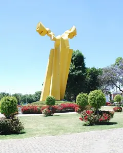 Ángel Custodio sculpture with bright yellow abstract forms in a landscaped park.
