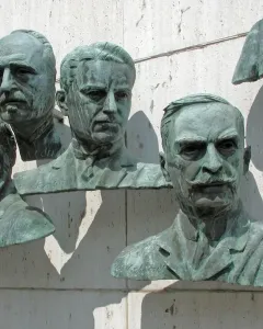 Four bronze busts from the Polio Hall of Fame mounted on a light stone wall, with part of a fifth bust visible.