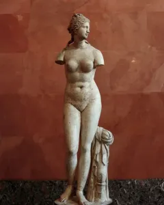 Venus Tauride marble statue with missing arms, standing beside a draped pillar.