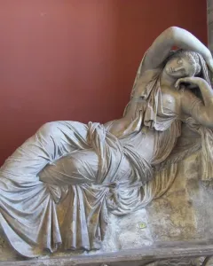 Sleeping Ariadne reclining in white marble with draped fabric and one arm raised over her head.