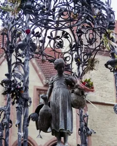 Gänseliesel Fountain bronze statue of a girl holding a goose and a basket of flowers beneath an ornate canopy.