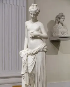 Pandora marble statue of a standing woman holding a small object, with drapery around her lower body.