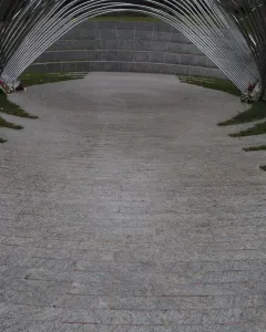 Infinite Wave memorial with arched metal bars forming a tunnel-like walkway beside a curved stone wall.