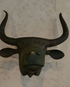 Toros de Costitx bronze bull head sculpture with curved horns and stylized features against a light wall.