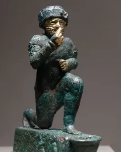 Worshipper of Larsa kneeling figure with a raised hand and gold details on an oxidized green surface.