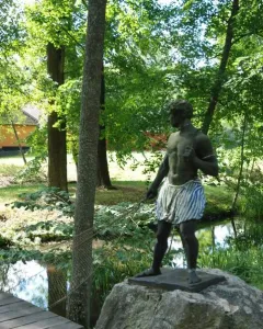 Morianbron sculpture standing on a boulder beside a stream with a rope and wooden walkway nearby
