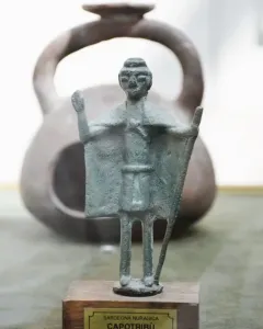 Nuragic bronze statuette of a tribal chief with a raised arm and staff, mounted on a wooden base.