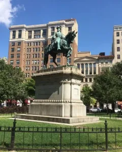 Major General James B. McPherson Memorial equestrian statue on a tall pedestal in a grassy park with city buildings behind it.