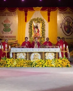 Black Nazarene statue in red and gold robes carrying a cross beneath a floral archway