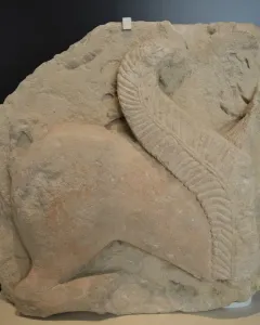 Weathered stone relief of the El Salobral Sphinxes shown in profile, with a large textured wing curving upward across the figure.
