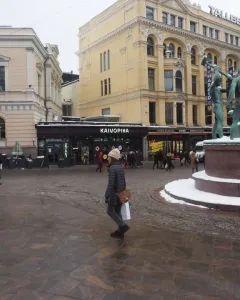 The Three Smiths sculpture on a snow-dusted pedestal in a busy Helsinki square.