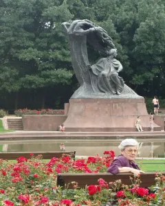 Chopin Monument in Warsaw surrounded by red roses, with people gathered around a reflecting pool.