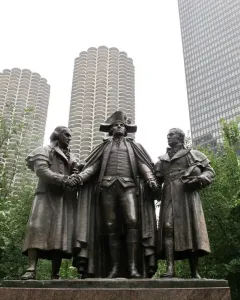 Heald Square Monument bronze sculpture of three historical figures on a red granite pedestal, with downtown skyscrapers behind it.