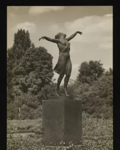 The Dancing Girl sculpture stands on a tall pedestal outdoors among trees.