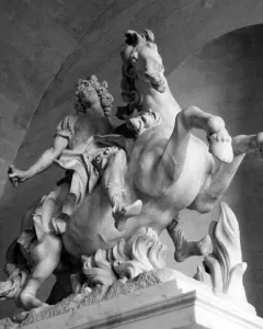 Equestrian Statue of Louis XIV shown as a marble rider on a rearing horse beneath a dark arched ceiling.