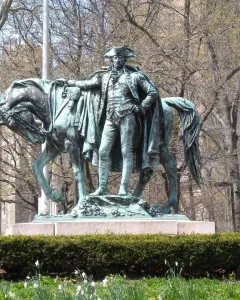 George Washington statue on a granite base with a horse beside it, framed by hedges and bare trees.