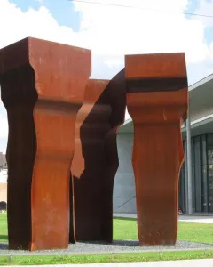 Buscando la Luz II sculpture with three tall rust-patinated metal forms on a grassy lawn.