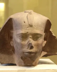 Weathered stone head of the Djedefre sphinx with a damaged nose and royal headpiece featuring a cobra emblem.