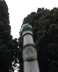 Lighthouse of Lierna, a tall stone monument with a green lantern top beside dense trees.