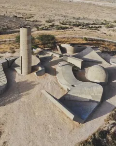 Aerial view of the Monument to the Negev Brigade, showing a concrete tower, curved walls, and geometric platforms on a dry landscape.