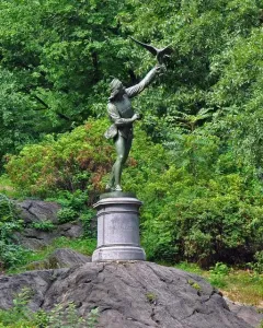 The Falconer bronze statue on a stone pedestal among trees in Central Park.