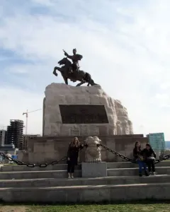 Statue of Damdin Sükhbaatar on a stone plinth with people posing on the steps below it.