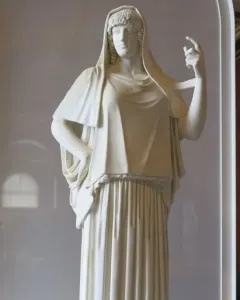 Giustiniani Hestia, a white marble statue of a standing woman in a long pleated robe with a mantle over her head and shoulders.