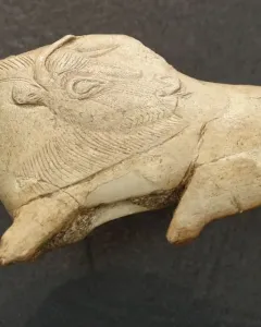 Carved bison figurine with its tongue extended, showing an engraved eye and textured fur details.