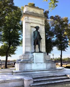 John Paul Jones Memorial with a bronze statue in a marble pylon against trees, water, and a distant bridge.
