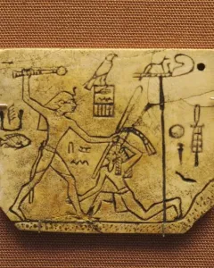 MacGregor plaque showing a crowned figure with a mace about to strike a kneeling figure, with hieroglyphs on the ivory surface.