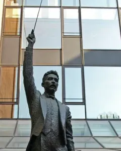 A Lluís Millet bronze statue holding a conductor’s baton aloft on a stone pedestal.