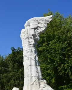 Monument to the Battle of Monte Cassino, a white marble abstract winged figure bound to a tall column in a garden.